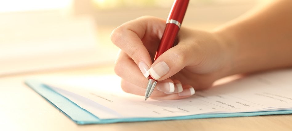 close-up of a hand writing with a pen on a financial aid form